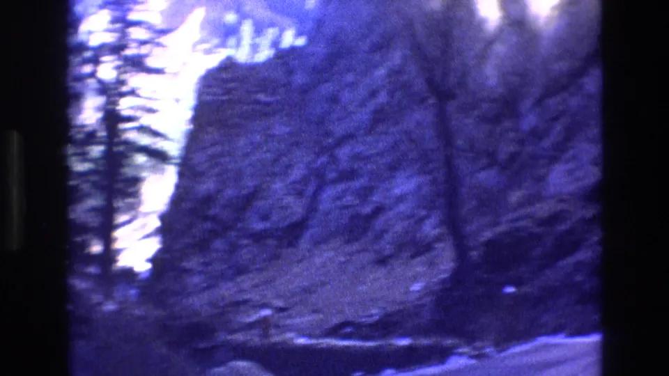 1973 Colorado 8mm frame looking across rocky mountainside terrain with trees, pale snow-like patches, and visible film-frame borders.