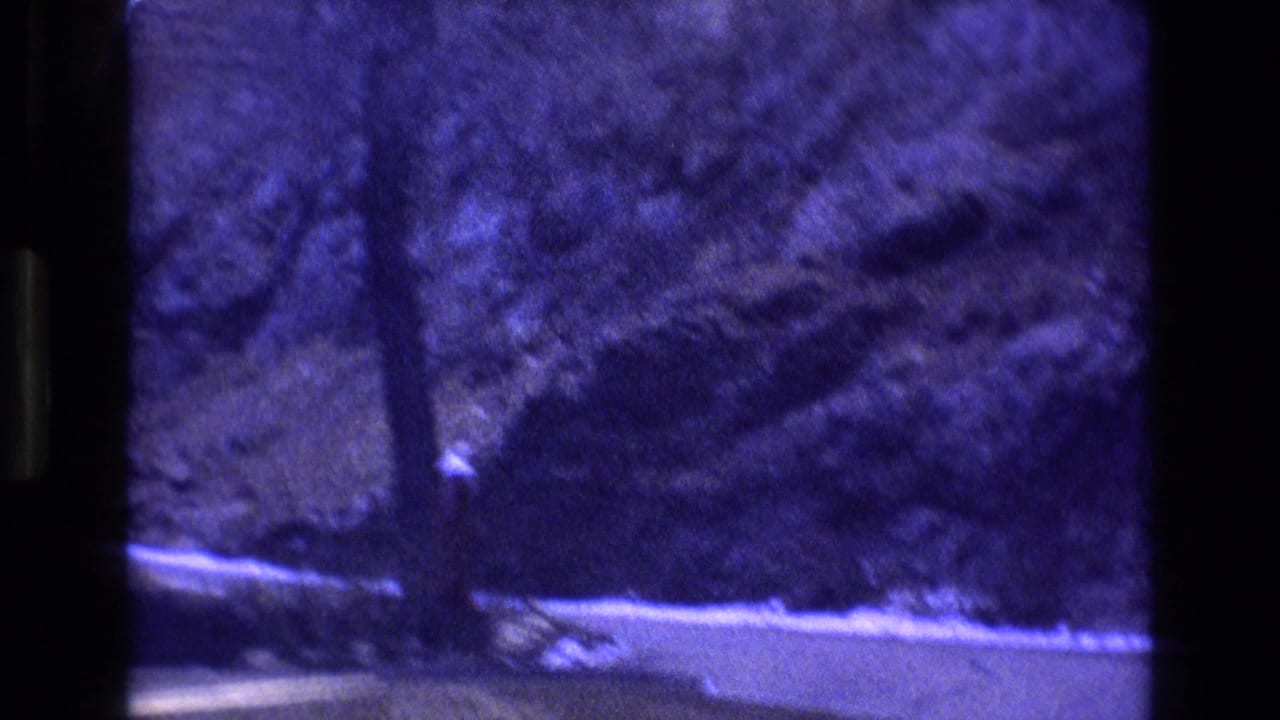 Winding mountain road beside snowy shoulder and dark rocky forest slope.