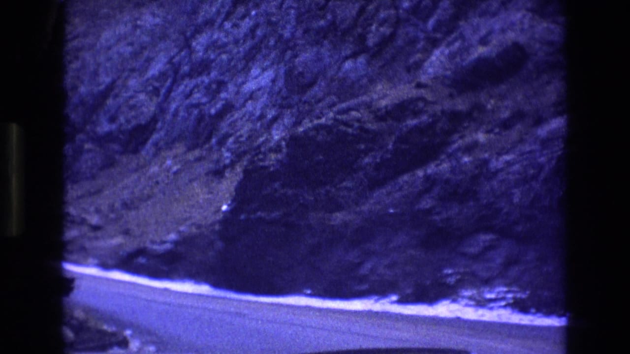 Road curving below a steep forested cliff with snow along the edge.