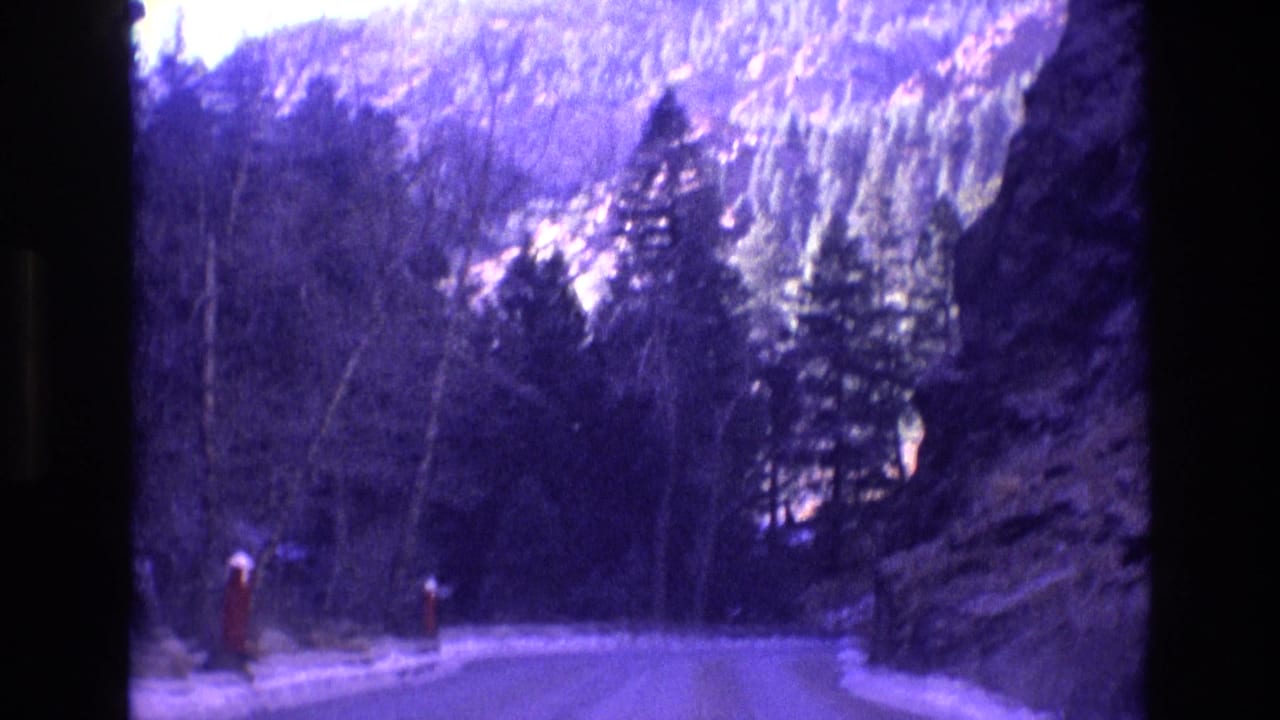 Snowy road curves through trees between rocky canyon walls.