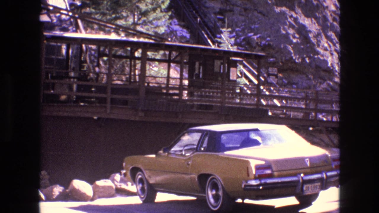 Gold 1970s sedan parked beside a rustic wooden structure in rocky terrain.