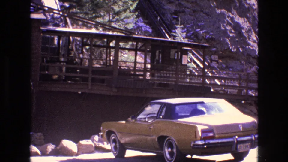 1973 Colorado 8mm frame showing a gold sedan near boulders and a rustic wooden structure set against rocky terrain and evergreens.