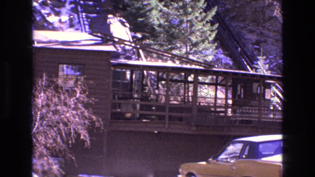 Wooden mountain lodge beside a yellow car with snowy hillside railway behind it.