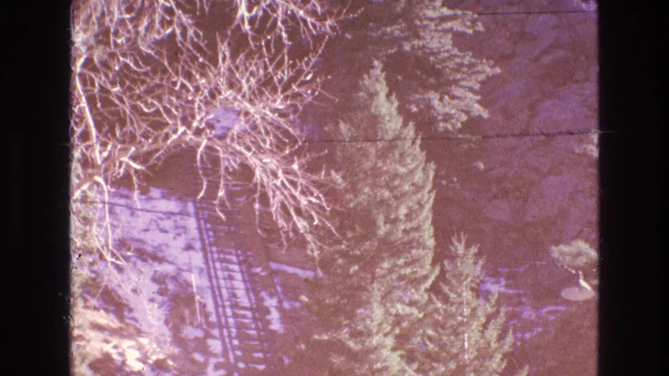 Faded 1973 Colorado 8mm frame showing snowy trees, incline railway tracks, bare branches, and a small lower platform or visitor area, with exposure and color shift visible.
