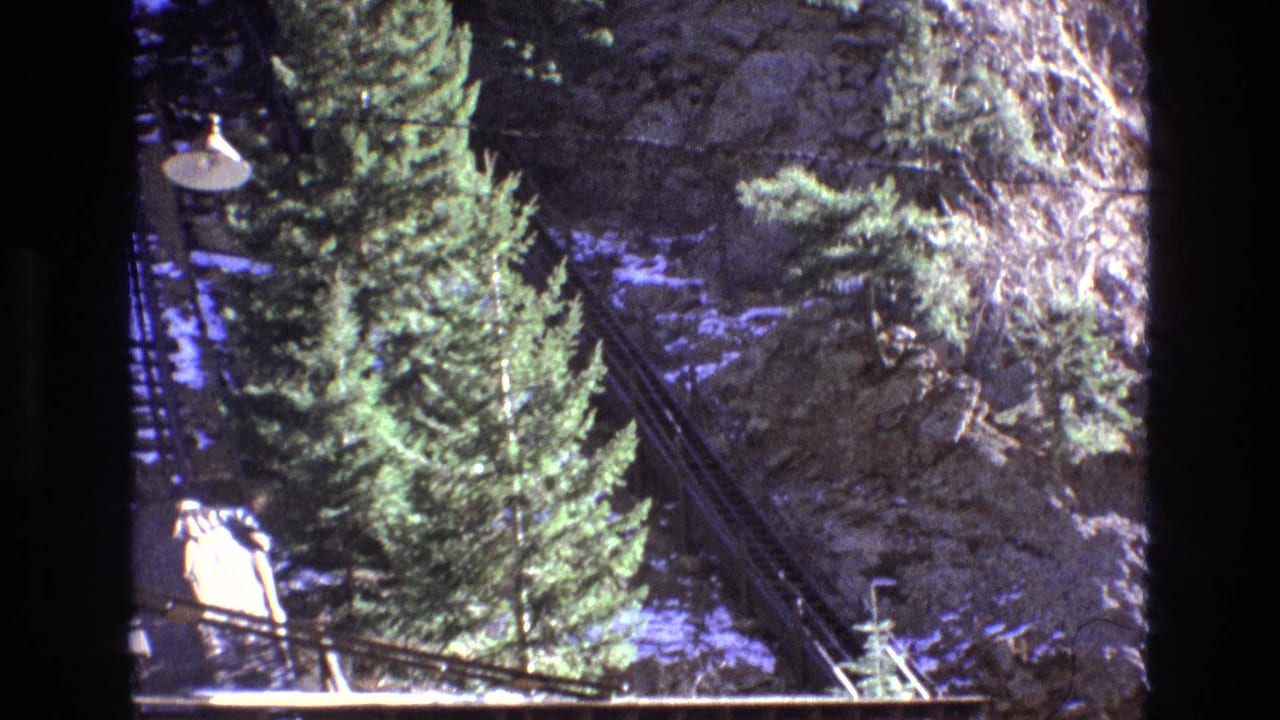 Wooden mountain railway platform beside evergreen trees and a rocky slope.