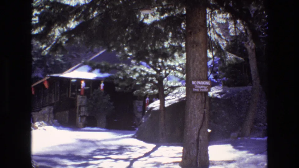 1973 Colorado 8mm frame showing a shaded forest path, a rustic structure, and a tree-mounted no-parking sign near a mountain attraction area.