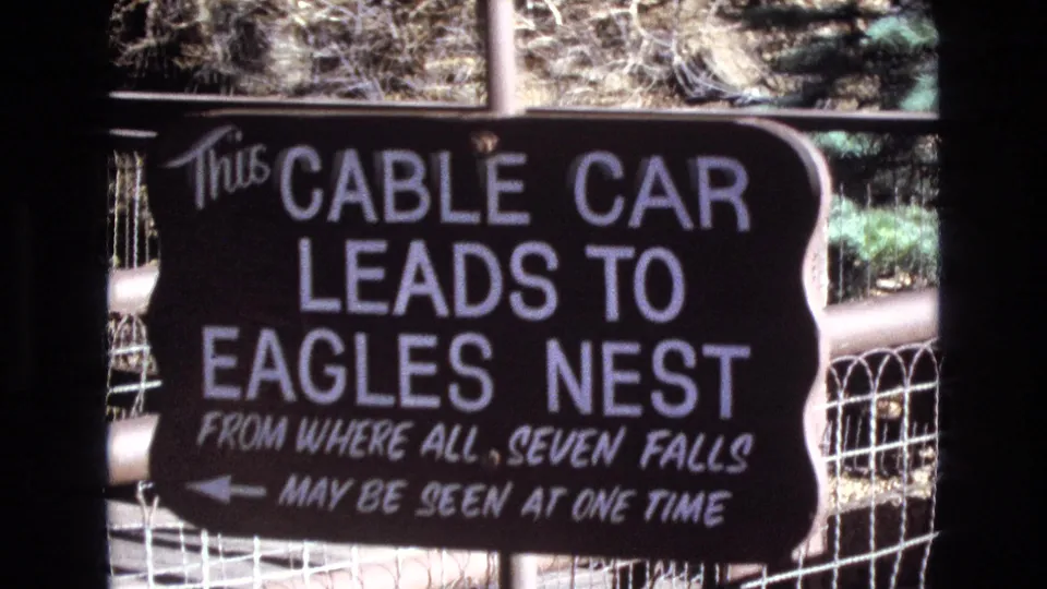 1973 Colorado home-movie frame of a tourist sign stating that the cable car leads to Eagles Nest, from where all seven falls may be seen at one time.