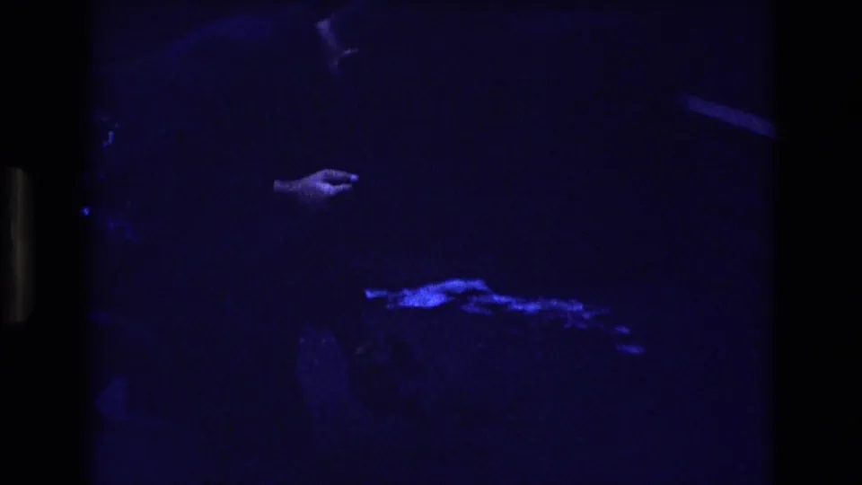 1973 Colorado 8mm frame in deep blue low light, showing a partially visible person reaching a hand toward a small bright object near the ground.