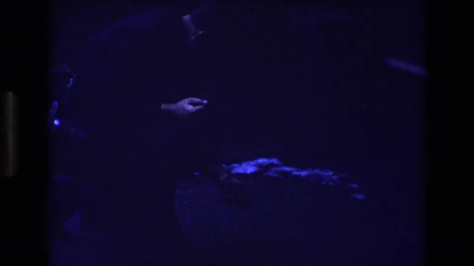 A blue-tinted 1973 Colorado home-movie frame shows a partially visible person and hand above a small glowing shape on the ground.