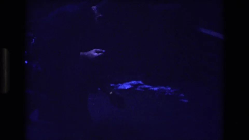 The final 1973 Colorado 8mm frame remains very dark, with a partial figure, a hand, and a small bright blue shape near the lower edge.