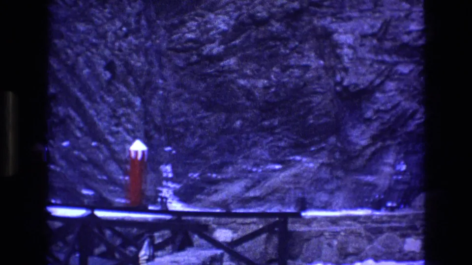 Blue-tinted 1973 Colorado 8mm frame showing one prominent red post capped with snow near a bridge or walkway and a rocky winter hillside.