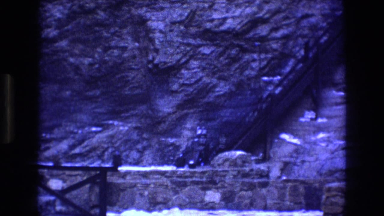 1973 Colorado 8mm frame showing a rocky mine site with a diagonal metal stairway or conveyor and a small person near the base of a stone retaining wall.