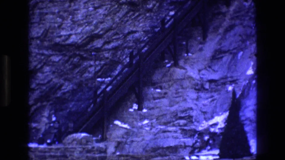 1973 Colorado 8mm frame showing the lower mine area with rough stonework, a diagonal metal structure, bright pale ground, and a person partly visible near the right side.