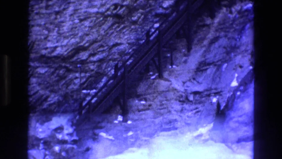 Final 1973 Colorado 8mm frame of the rugged mine site, showing the diagonal industrial structure against a rock wall with bright overexposed ground and dark film borders.