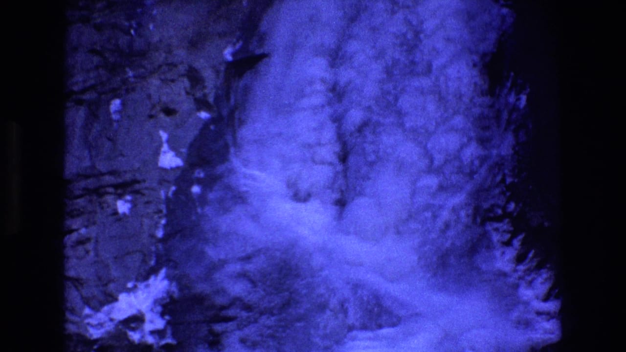 1973 Colorado 8mm frame showing what appears to be blue-tinted fog or cloud billowing against a dark rocky mountainside or valley wall.