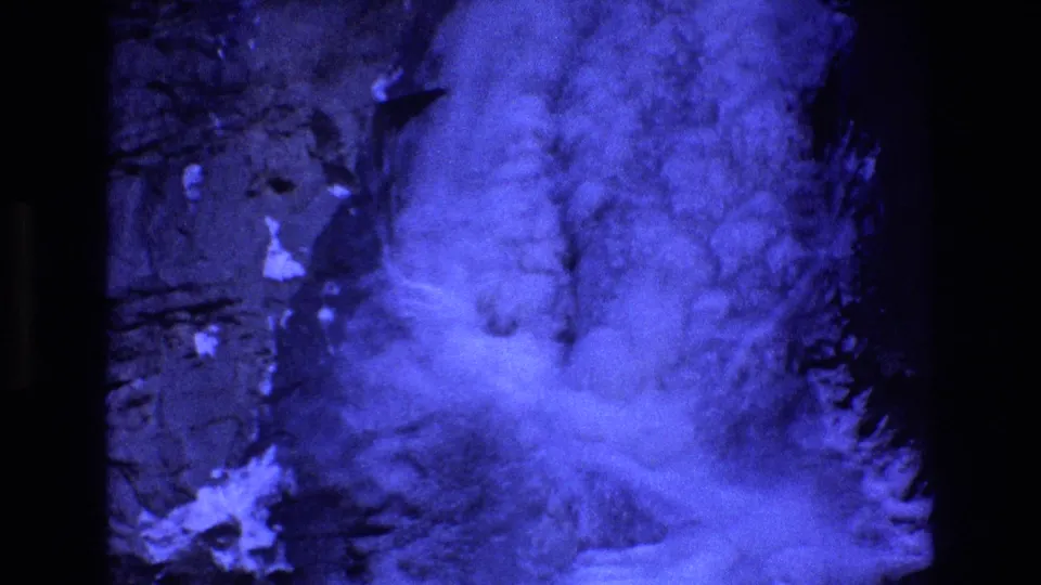 1973 Colorado 8mm frame showing what appears to be blue-tinted fog or cloud billowing against a dark rocky mountainside or valley wall.