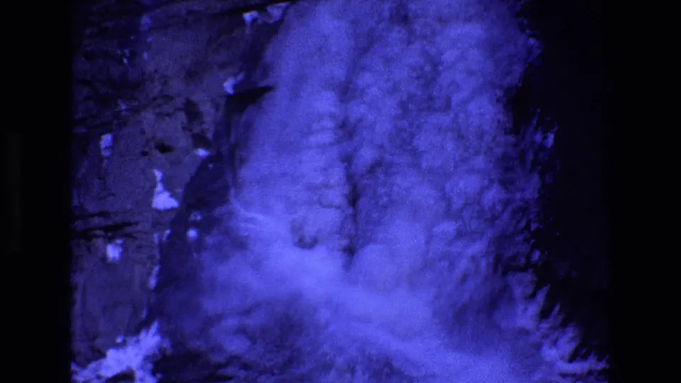 Blue-cast 8mm frame from Colorado in 1973, with dense mist or cloud shapes drifting across a dark rocky valley backdrop.