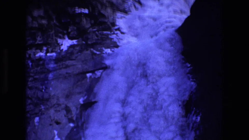Blue-tinted 8mm frame from the Colorado clip, showing a swirling fog or cloud mass set against a shadowed rocky valley surface.