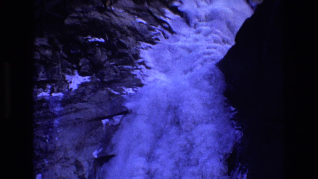 1973 Colorado 8mm frame showing turbulent water cascading through a dark rocky mountain gorge with part of a wooden walkway above the flow.
