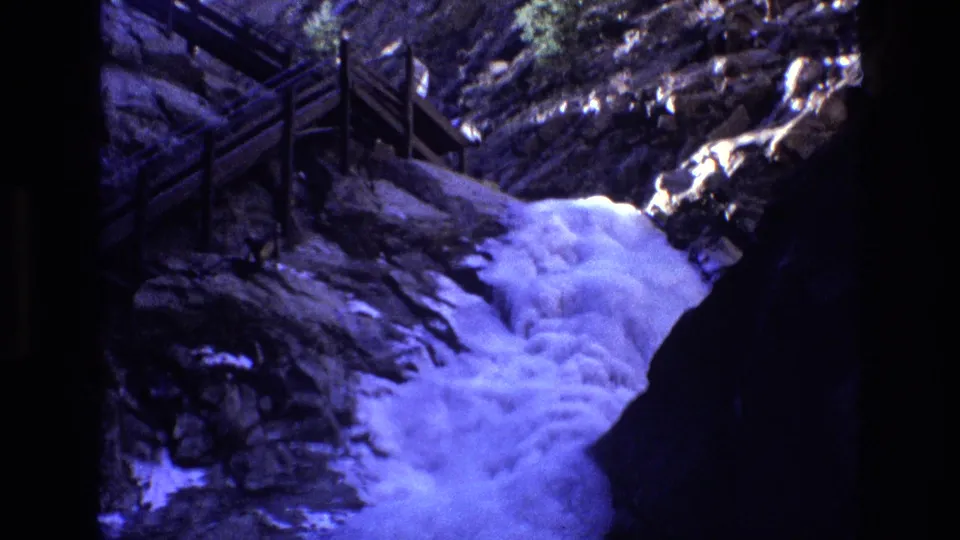 1973 Colorado 8mm frame showing a scenic wooden walkway crossing or following a rocky gorge while foaming blue-white water cascades below.