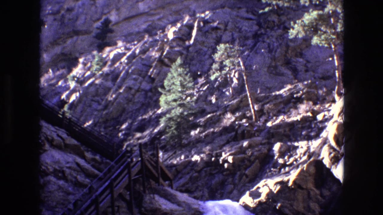 Wooden stairway beside a rocky canyon waterfall with evergreen trees above.