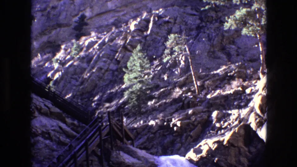 1973 Colorado 8mm frame showing a steep wooden stairway and railing along dark rock beside rushing water in a narrow mountain canyon.