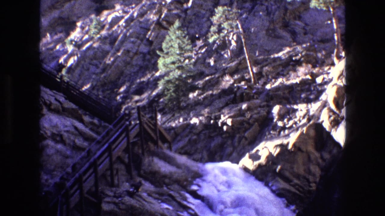 Steep rock formation with railing and white water flowing through the canyon.