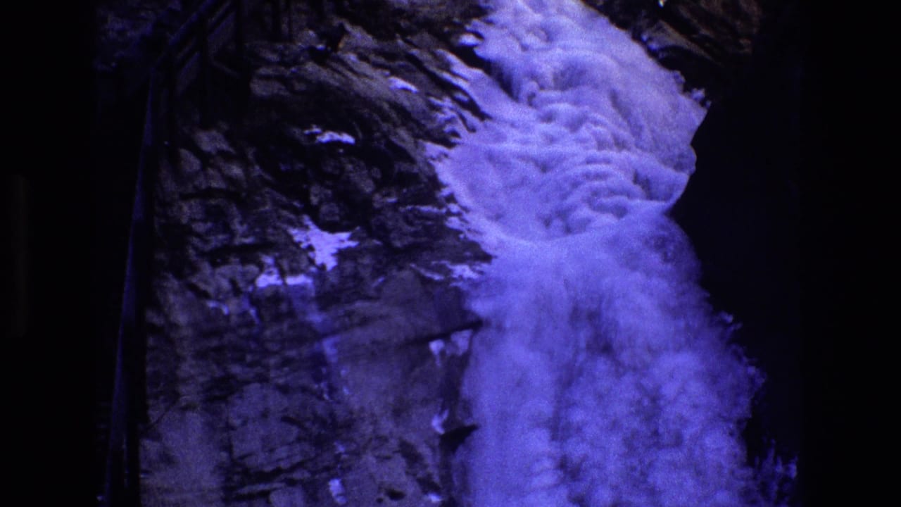 Close view of blue-toned waterfall descending beside dark rock.
