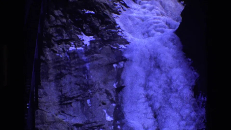1973 Colorado home-movie frame showing a foamy waterfall against dark, snow-dusted rock, with the scene held from a steady visitor viewpoint.