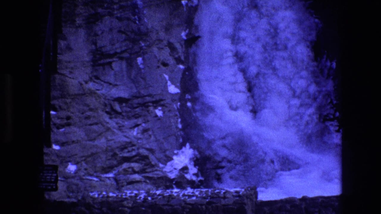 Waterfall and spray against a dark rocky wall with snow along the lower edge.