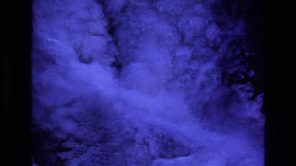 1973 Colorado home-movie frame showing dense blue ice and frozen spray at the base of a waterfall, bordered by dark rock and deep shadows.