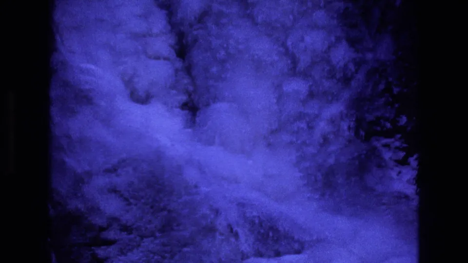 1973 Colorado 8mm frame with a blue night-filter look, showing turbulent snow texture on a steep slope framed by dark film borders and shadowed terrain.