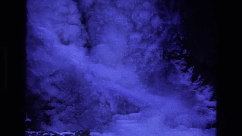 1973 Colorado 8mm frame showing blue-filtered snow movement against dark mountain forms, with soft focus, high contrast, and visible frame-edge artifacts.
