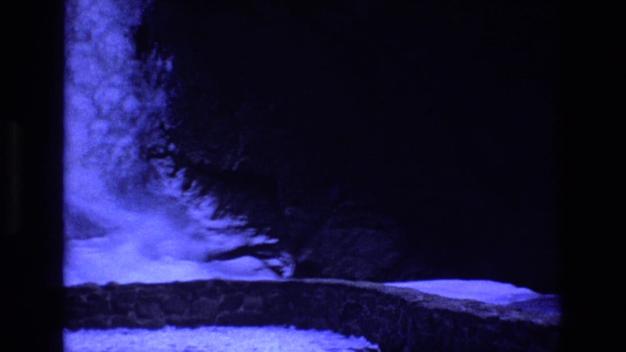 Colorado 1973 8mm frame showing a blue-lit rocky ledge or cave-like wall with deep shadows and black frame edges, before the model rocket is clearly centered.