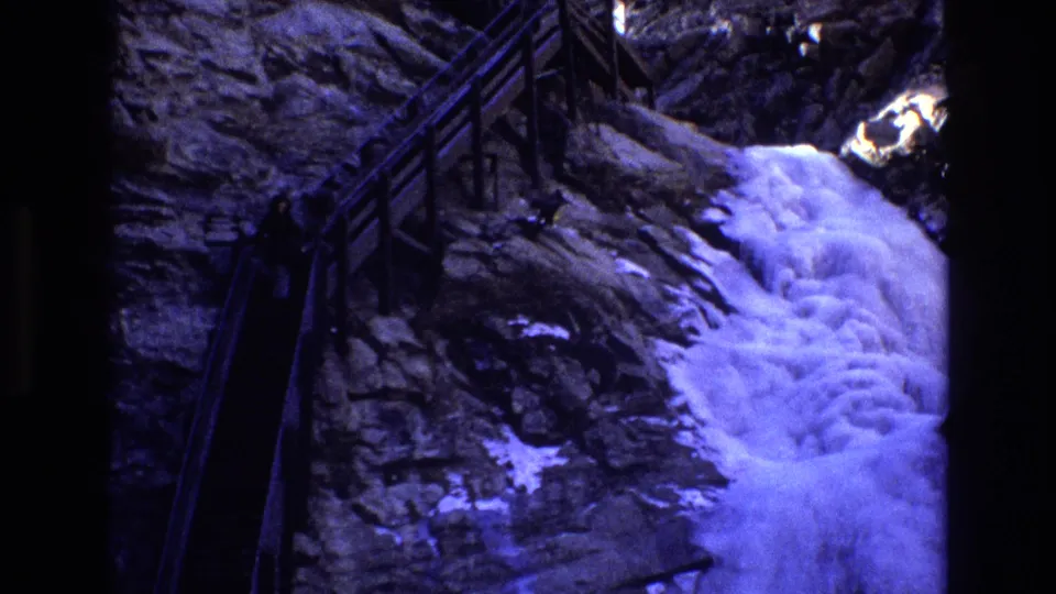1973 Colorado 8mm frame showing the railed cliffside stairs and bright foaming cascade in a blue-purple home-movie exposure.