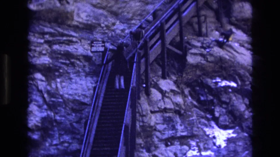 1973 Colorado 8mm frame showing a distant tourist in dark outerwear climbing the narrow railed stairs built into the rock face.