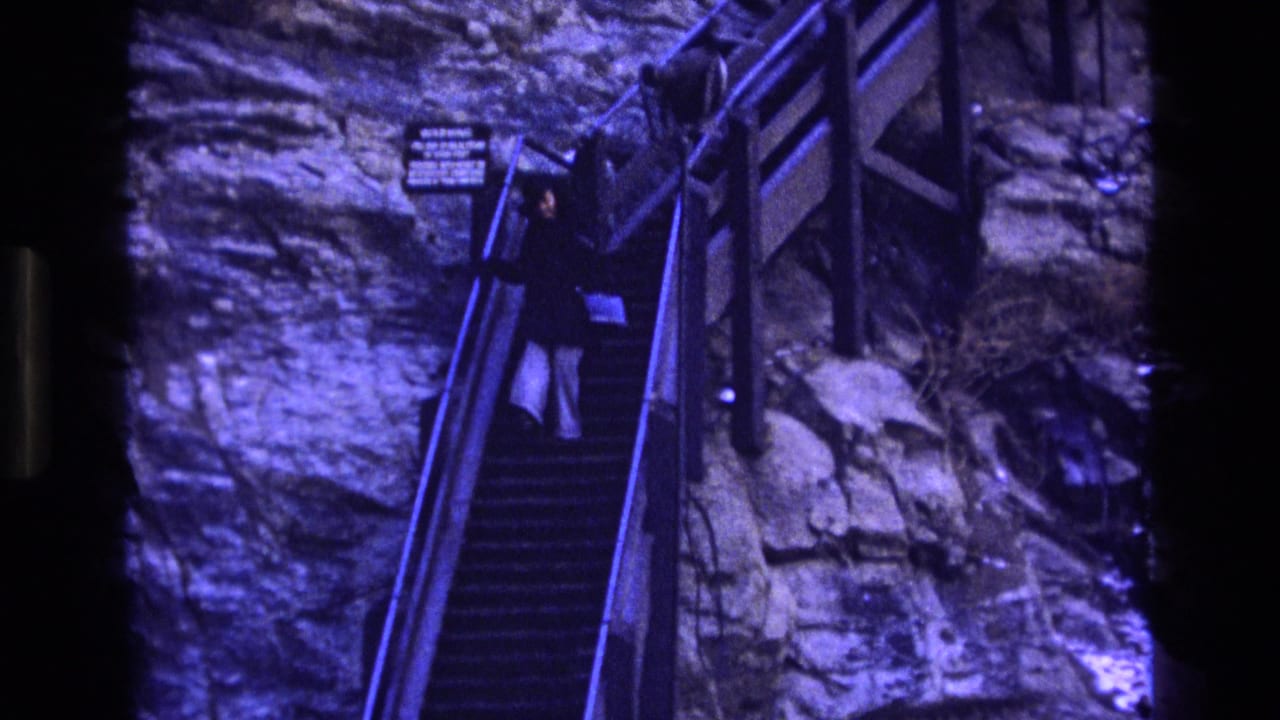 Woman descends a steep stairway along a rocky wall with railings.