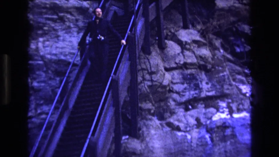 Close 1973 Colorado travel frame of an adult descending toward the camera on a narrow staircase bordered by rough cliff rock.