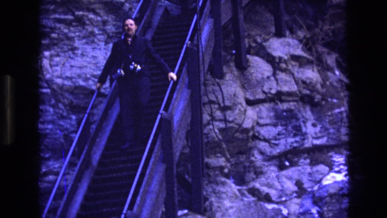 Man holding a railing while walking down stairs beside a rock wall.