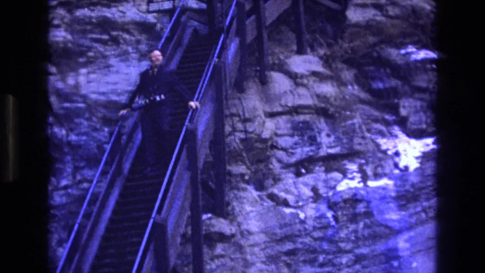 Motion blur and blue-tinted 8mm texture show the man continuing down the steep stairway beside rough Colorado rock formations.