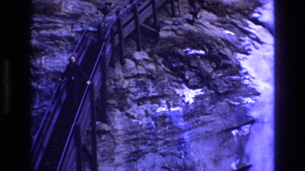 1973 Colorado 8mm frame showing an adult in dark winter clothing descending a steep stairway built along a rocky, snowy cliffside.