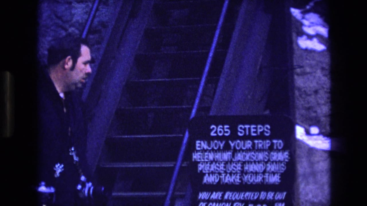 In 1973 Colorado 8mm footage, an adult man in a dark jacket stands near a stone stairway and a sign for the 265 steps to Helen Hunt Jackson's Grave.