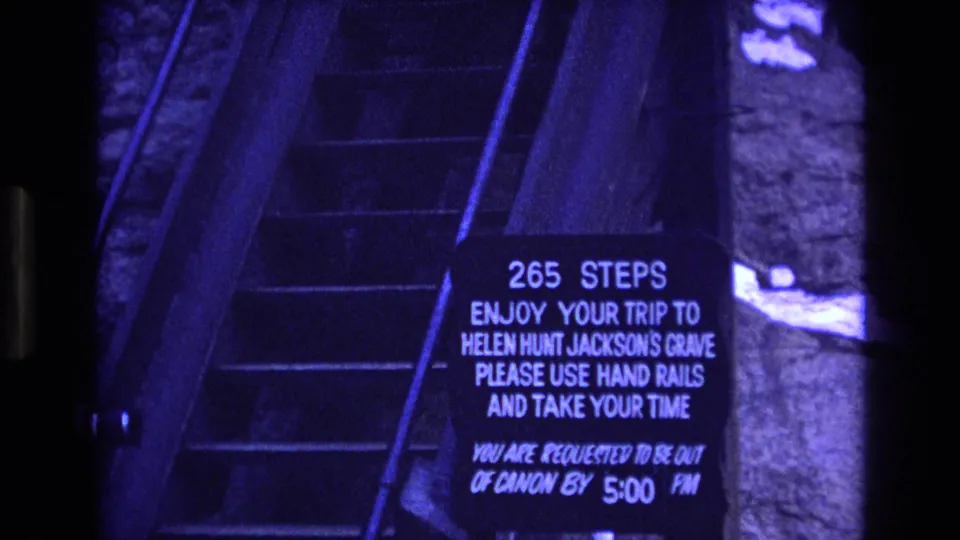 The frame centers on the stone stairs and posted visitor sign for Helen Hunt Jackson's Grave, with no person clearly visible in this sampled frame.