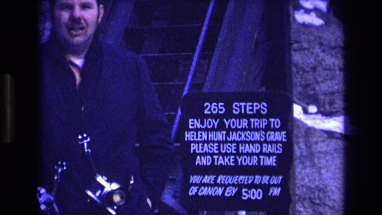 1973 Colorado 8mm frame showing an adult man with a camera standing near stairs and a sign marking 265 steps to Helen Hunt Jackson's grave.