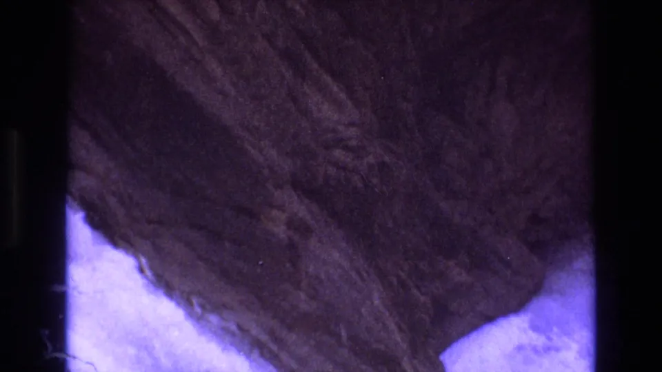 1973 Colorado 8mm frame ending on a close view of rugged rock texture beside pale ground, with the aged film's purple-blue cast still visible.