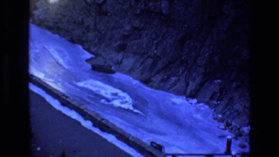 1973 Colorado 8mm frame with a winding river below snow-covered banks and steep rocky canyon terrain, seen during the camera pan.