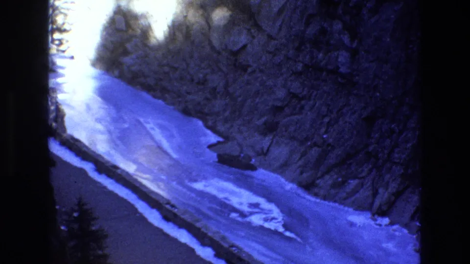 1973 Colorado 8mm frame looking along a snowy canyon river, with rocky cliffs, trees, and a small roofed structure near the bank.