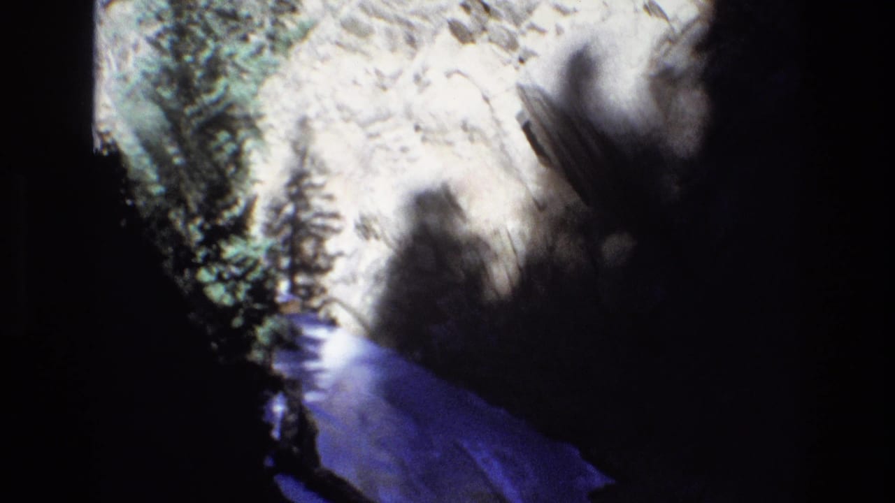 Rocky slope with pine trees and a blue-tinted stream below.