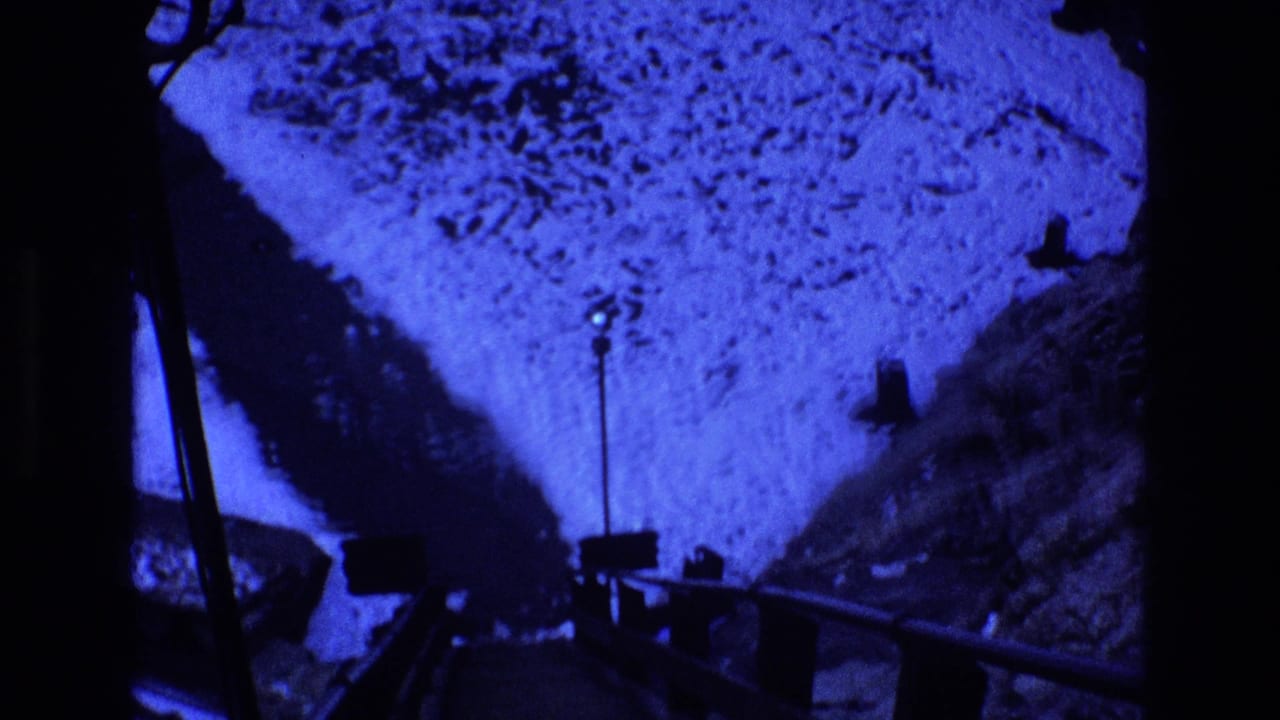 Blue-shifted 1973 Colorado 8mm frame showing snow-covered ground, a dark bridge or walkway edge, and a small lamp post in a nighttime mountain setting.