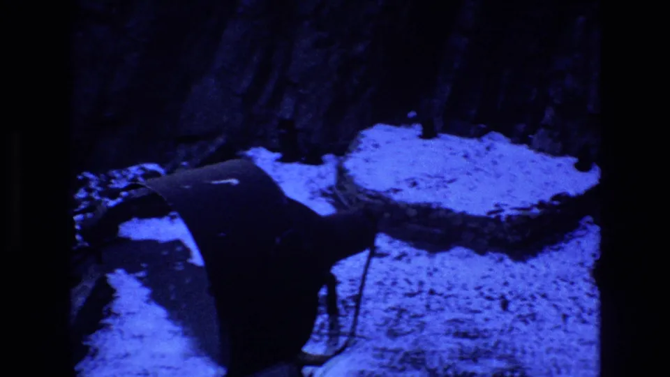 Final 1973 Colorado 8mm frame showing snow, a dark angular bridge or walkway surface, and shadowed outdoor terrain under a strong blue night cast.